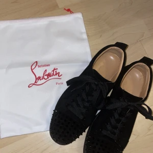 Svarta sneakers från Christian Louboutin - Snygga svarta sneakers från Christian Louboutin med den ikoniska röda sulan. Skorna har snörning och är dekorerade med nitar på tån för en edgy look. Perfekta för att ge din outfit en lyxig touch. Skorna är såklart äkta, kvitto,box,dustbag,nitar,snöre osv följer med. Säljes pga av att dem är för stora för mig. För mer bilder eller info så är det bara att höra av er!