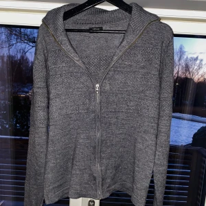 Grå stickad cardigan från Milano - Säljer en stilren grå stickad cardigan från Milano. Tröjan har en dragkedja framtill och långa ärmar. Perfekt för kyligare dagar med sin mjuka och bekväma passform.