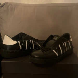 Svarta sneakers från Valentino - Snygga svarta sneakers från Valentino med vit logga på sidan. Skorna har en klassisk design med snörning och är tillverkade i skinn. Perfekta för en stilren look.
