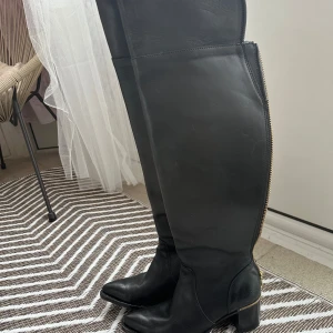 Primeboots cowboy stil  - Snygga svarta stövlar från Primeboots i skinn med guldiga dragkedjor längs sidan. De har en klack och spetsig tå, vilket ger en elegant look. Perfekta för att lyfta vilken outfit som helst. 