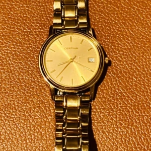 Guldfärgad klocka från Certina - Snygg guldfärgad klocka från Certina med datumvisning. Armbandet och boetten är i rostfritt stål, vilket ger en elegant och tidlös look. Perfekt för den som vill ha en stilren accessoar.