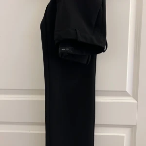 Svarta kostymbyxor från Vero Moda - Eleganta svarta kostymbyxor från Vero Moda. Perfekta för en stilren look med en klassisk passform. Byxorna har bälteshällor och en diskret dragkedja framtill.