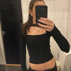 Svart ribbad långärmad topp - Snygg svart ribbad topp med lång ärm och unik cut-out design vid halsen. Perfekt för en stilren look.