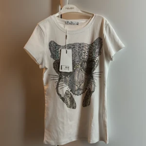 Vit t-shirt med paljettdetalj från May by Shining Star - Snygg vit t-shirt från May by Shining Star med en cool paljettdekoration i form av ett djurmotiv på framsidan. Perfekt för att ge din outfit lite extra bling! 👕✨