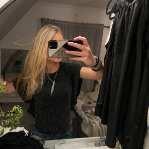 Svart glittrig topp - Snygg svart glittrig topp med korta ärmar och en croppad passform. Perfekt för en kväll ute eller en festlig tillställning. Toppen har en rund halsringning och ger en stilren look.