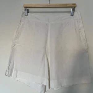 Linneshorts, Bondelid, ”Ellens shorts”, M, vita - Vita linneshorts från Bondelid (MQ), modell ”Ellen shorts”, i storlek M. Shortsen är i nyskick.  Högmidjade. Vid passform. Pressveck fram och bak. Fickor på sidorna. Stängs med dold dragkedja på ena sidan. 100% linne.   Mått: Yttre längd ca 46 cm Inre längd ca 16 cm Midja ca 17,5 cm Stuss ca 52 cm
