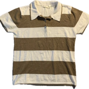 Randig pikétröja i beige och vit - Säljer en stilren randig pikétröja i beige och vit. Tröjan har korta ärmar och en klassisk krage med knappar framtill. Perfekt för en avslappnad stil. Finstickad i viscose och nylon. Står storklek large men skulle säga att den sitter som en s/m