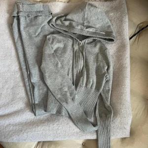 Grå hoodie med dragkedja - Säljer en stilren grå hoodie med dragkedja och huva. Tröjan har ribbade muddar vid ärmslut och nederkant, vilket ger en snygg passform. Perfekt för en avslappnad look, med tillhörande under del med fin detalj Väldigt fint skick 
