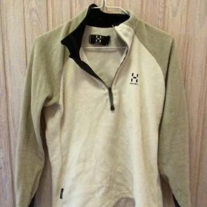Beige fleece tröja från Haglöfs - Säljer en supermysig beige fleece tröja från Haglöfs. Perfekt för kyliga dagar med sin halvdragkedja och mjuka material. Den har en stilren design med svart krage och Haglöfs-logga på bröstet. Passar perfekt för höst- och vinteräventyr! 🍂❄️