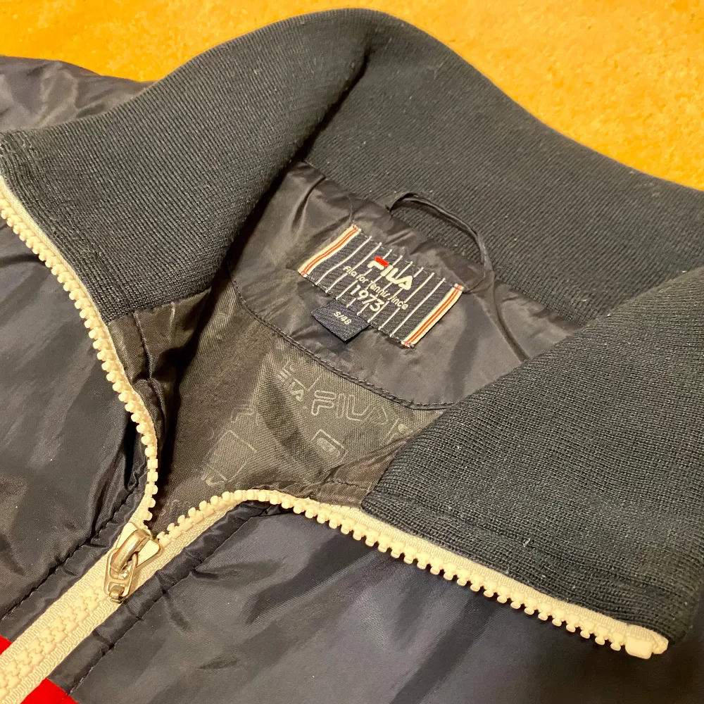 Säljer en snygg retro blå jacka från Fila med vita och röda detaljer. Jackan har en dragkedja framtill och två fickor med dragkedjor. Perfekt för höst och vinter, med en retro look och bekväm passform. Den är i mycket bra skick och redo för nya äventyr! Storlek S - se bilder för mått.. Jackor.