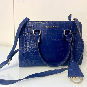 Blå axelväska från Michael Kors - Snygg blå axelväska från Michael Kors i krokodilpräglat skinn. Väskan har gulddetaljer och en praktisk dragkedja upptill. Perfekt för både vardag och fest! 💙