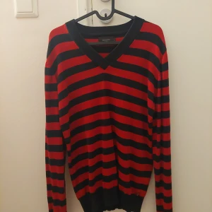 Svart röd randig tröja - Säljer en mörkröd-svart randig tröja. Den har en v-ringad hals och långa ärmar, perfekt för höst och vinter. Tröjan är i gott skick!
