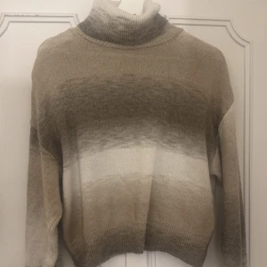 Beige och vit polotröja - Säljer en supermysig polotröja i beige och vit med en snygg ombre-effekt. Perfekt för kyliga dagar med sin stickade design och långa ärmar. Tröjan har en bekväm passform och ribbade kanter som ger extra stil. Passar perfekt till både jeans och kjol!