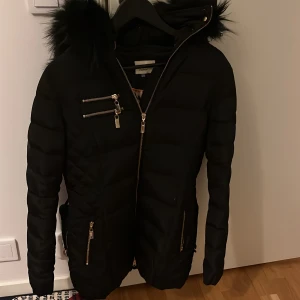 Svart pufferjacka med pälsdetaljer - Säljer denna Roco baroco jackan, använd ungefär 1 vinter.