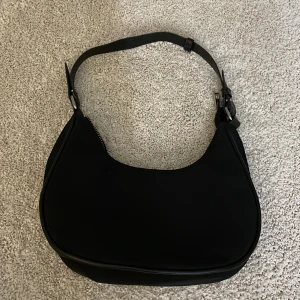 Svart axelväska från Sinsay - Snygg svart axelväska från Sinsay i syntetmaterial. Den har en praktisk dragkedja och en dragkedja inuti också. Perfekt för vardagsbruk eller en kväll ute. Enkel och stilren design som passar till allt! Pris kan diskuteras!!