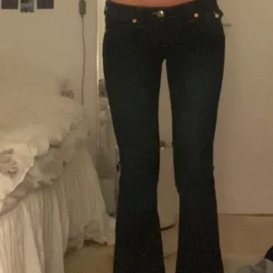  bootcut jeans från True Religion - Säljer ett par snygga mörkblå bootcut jeans från True Religion. De är i nytt skick, m lapp kvar och alldrig använda. De har en klassisk femficksdesign med guldfärgade knappar och nitar. Perfekta för både vardag och fest! 🖤