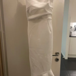 Vit klänning från ASOS - Säljer en elegant vit klänning från ASOS i nytt skick. Materialet känns lyxigt och klänningen har en tight passform som framhäver figuren. Den är axelbandslös och har en lång längd som ger en sofistikerad look.