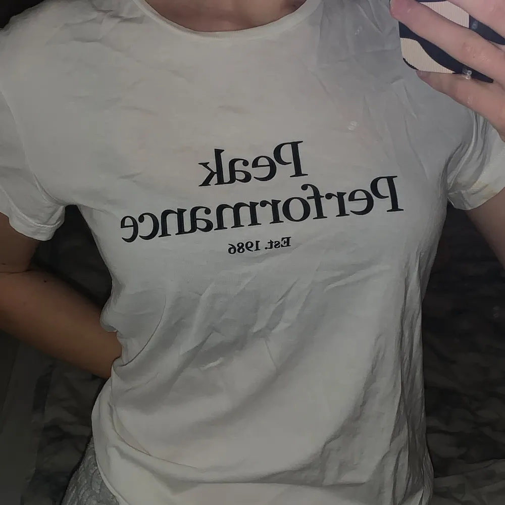Säljer en vit t-shirt med texten 'Peak Performance Est. 1986' tryckt på framsidan. Den är i bra skick och har en normal passform.. T-paidat.