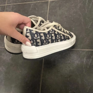 Christian Dior sneakers (intressekoll) - Säljer ett par snygga Christian Dior sneakers i mycket bra skick. De har ett coolt mönster i blått och vitt med märkets logga. Skorna har snörning och en bekväm vit sula. Perfekta för att ge din outfit en lyxig touch! Har tyvärr inget kvitto! för att ja köpte skorna av en annan tjej på Plick. 