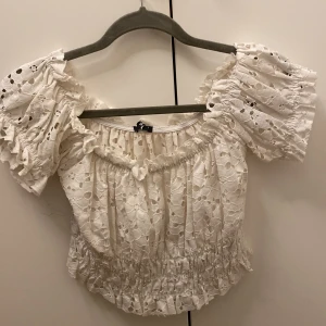 Vit spetsblus från Gina Tricot - Säljer en superfin vit spetsblus från Gina Tricot i storlek S. Blusen har korta puffärmar och en elastisk midja för en bekväm passform. Perfekt för sommarens alla fester eller en dag på stan. 🕊️