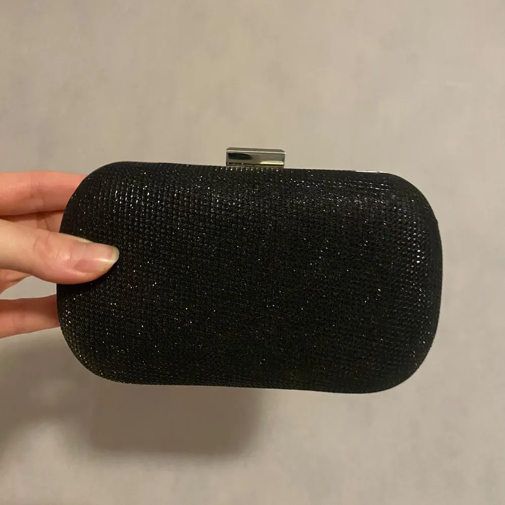Snygg svart kuvertväska från Karen Millen med glittrig yta och silverfärgad ram. Perfekt för festliga tillfällen! Väskan har en smidig stängning och är i mycket bra skick. En stilren accessoar som passar till många outfits. Utan axelband. . Laukut & Käsilaukut.
