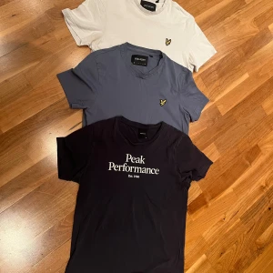 Tre t-shirts från Lyle & Scott och Peak Performance - Säljer tre snygga t-shirts i olika färger. Två från Lyle & Scott i vit och blå med deras ikoniska logga, och en mörkblå från Peak Performance med tryck. Perfekta för vardagsbruk eller träning. Alla är kortärmade och i bra skick.