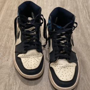 Nike Air Jordans i blått och vitt - Säljer ett par Nike Air Jordans i blått och vitt. Skorna har en klassisk hög modell med snörning och är i bra skick. Perfekta för både vardag och fest! De har en snygg kombination av blå, vit och svart färg med en robust sula för bra grepp.