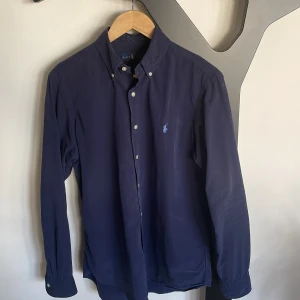 Ralph Lauren skjorta - Snygg och trendig marinblå skjorta från Polo Ralph Lauren. Storleken är medium och modellen på bilden är 183cm och 78kg. Skjortan är använd, men i fortsatt bra skick. Nypris 1700kr.