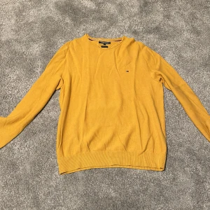 Gul tröja från Tommy Hilfiger - Säljer en snygg gul tröja från Tommy Hilfiger i premium bomull. Den har en klassisk design med rund hals och långa ärmar. Perfekt för både höst och vår. Tröjan är i storlek XL och har en liten logga på bröstet. Superbekväm och stilren!