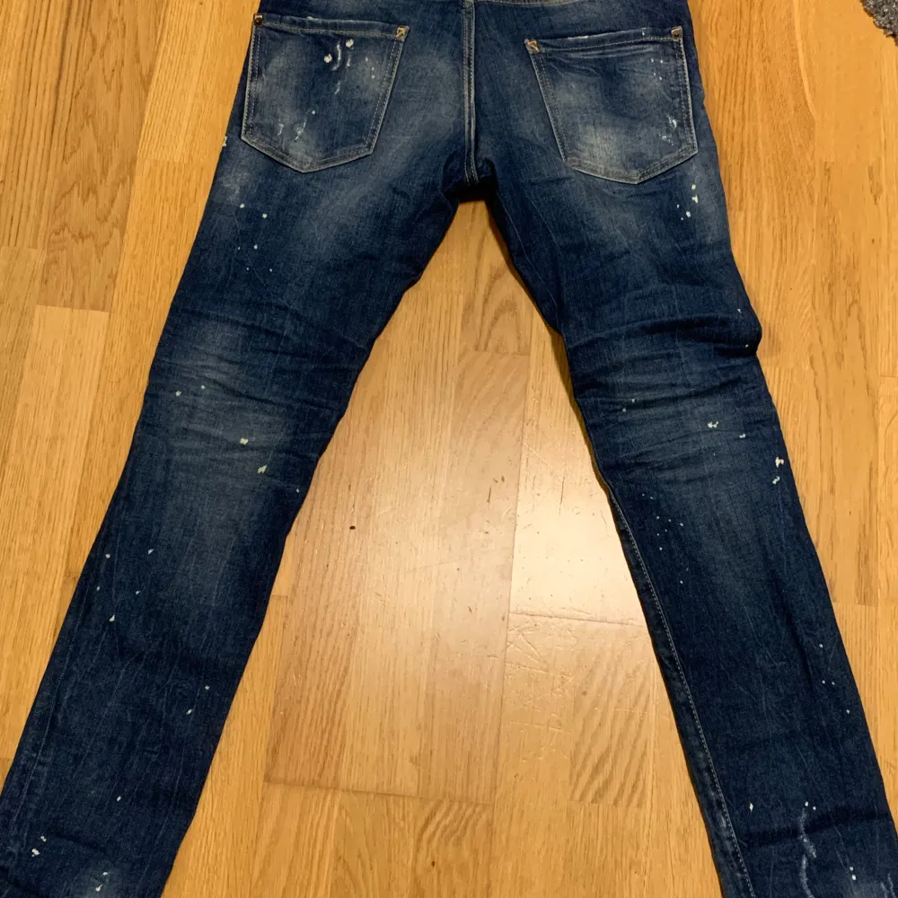 Säljer ett par mörkblå jeans med coola slitningar och en vintage look. De har en snygg tvättad effekt och små färgstänk som ger dem en unik stil. Perfekta för en avslappnad vardagslook! Storlek är barn storlek som är 14 years old.. Jeans & Byxor.