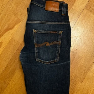 Nudie Jeans - Säljer ett par snygga mörkblå jeans, modell Taped Ted i storlek W32 L32 från Nudie. Har blivit lagade i grenen av Nudie Repair och inte använda sedan dess, dock syns inte denna lagning när man har på sig jeansen. Skickas eller möts upp i Sthlm.