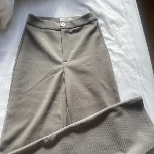 Kostymbyxor - Gråa ribbade kostymbyxor.  Höga i midjan och vida i benen.  Byxorna är gråa men kan upplevas som beiga/bruna på bilderna. 