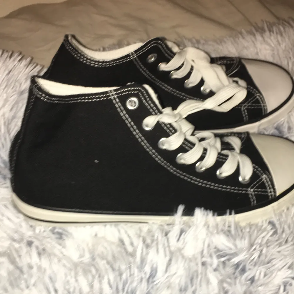 Säljer ett par klassiska svarta sneakers med vita snören och sulor. De har en enkel och stilren design med vita sömmar som kontrast. Perfekta för vardagsbruk och passar till det mesta i garderoben.. Skor.