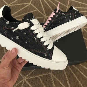 Svarta Numeris sneakers med stjärndetaljer - Säljer ett par svarta sneakers från Numeris med vit sula och slitna stjärndetaljer i tyget. Skorna har kontrasterande sömmar, vita och rosa skosnören samt en chunky sula. Materialet är denim-liknande tyg och insidan är svart. Perfekta för dig som gillar unik streetstyle.