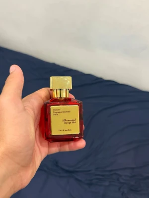 Baccarat Rouge 540 Eau de Parfum - Lyxig parfymflaska i rött glas med guldfärgat lock och etikett. Doften är Baccarat Rouge 540 Eau de Parfum från Maison Francis Kurkdjian, känd för sin unika och exklusiva karaktär. Flaskan har en elegant, fyrkantig form och känns riktigt premium. Parfymen kommer även med paket !