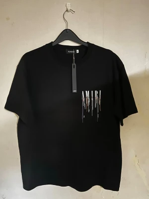 Amiri T-shirt - Säljer en svart t-shirt från AMIRI i storlek M. T-shirten har ett vitt tryck med droppande effekt på bröstet och klassisk rund hals. Tillverkad i mjuk bomull och har korta ärmar. Perfekt för dig som gillar streetwear och stilrena detaljer.
