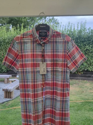 Rutig kortärmad skjorta från Bondelid - Säljer en färgglad rutig skjorta från Bondelid med korta ärmar och klassisk krage. Skjortan har knappar framtill och är i en tailored fit-modell. Färgerna går i rött, blått, vitt och inslag av grönt. Perfekt för dig som gillar en avslappnad men snygg stil.