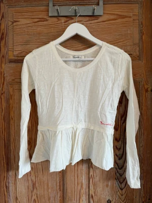 Vit långärmad blus från Bondelid - Söt vit långärmad blus från Bondelid med volang nedtill och rund halsringning. Perfekt för en avslappnad och stilren look.