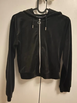 Svart velourhoodie med dragkedja - Svart hoodie i mjuk velour med hel dragkedja framtill och huva med snören. Långa ärmar och ribbade muddar vid ärmslut och nederkant. Perfekt för en chill och stilren look. Passar perfekt med byxorna från annonsen efter!!