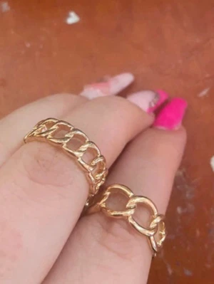 Guldfärgade kedjeringset - Två snygga guldfärgade ringar med kedjelänk-design. Ringarna har en öppen struktur och är tillverkade i metall med glansig finish. Perfekt för att ge din look en trendig touch.