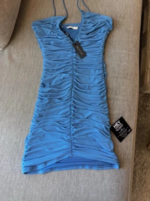 Blå ruched kortklänning NLY One - Supersnygg blå kortklänning från NLY One med ruched effekt längs hela klänningen. Klänningen har smala axelband och en tight passform som framhäver figuren. Perfekt för dig som vill sticka ut med en trendig look.