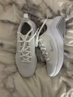 Vita Nike Air Zoom sneakers - Snygga vita Nike Air Zoom sneakers med mesh-ovandel och diskreta grå detaljer. Skorna har en låg siluett, klassisk snörning och en bekväm sula med tydlig Air Zoom-text på hälen. Perfekta för dig som gillar stilrena och sportiga sneakers.