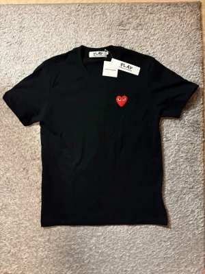 Comme des garçons t shirt - Säljer nu denna svarta t shirt med rött hjärta från märket commes des garçons. Tröjan är helt ny och är i perfekt skick. Storleken är S och skulle säga att den passar runt ~175cm. Skriv vid fler frågor! 