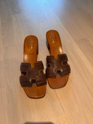 Bruna slip-in sandaler med klack - Köpta på Sicilien, äkta läder handgjorda i Italien. Snygga bruna slip-in sandaler med breda läderremmar i ett coolt geometriskt mönster. Sandalerna har en låg träklack och öppen tå. 