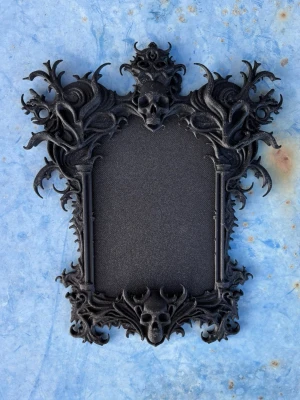 Victorian Gothic Skull Frame - Details:  ▫ Size: 12.7x15 cm / 5x5.9 inches ▫The frame is suitable for a photo of: 6.5x10.5 cm / 2.6x4.1 inches ▫ Material: 3D-printed PLA plastic ▫ Lightweight ▫ Shipped with double-sided tape   Important  Due to the nature of 3D printing, minor imperfections may occur, which are inconspicuous and do not significantly affect the overall quality of the product. To maintain the quality and appearance of a 3D-printed product, avoid exposure to extreme temperatures, humidity, direct sunlight