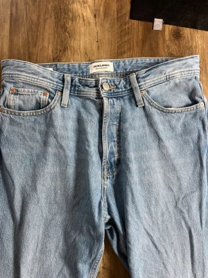 Ljusblå relaxed jeans från Jack & Jones - Säljer ett par ljusblå relaxed fit jeans från Jack & Jones, modell Chris. Klassisk femficksdesign, raka ben och hög midja. Tillverkade i slitstark denim med snygga kontrastsömmar. Perfekta för en avslappnad och trendig look. 100 cm från midjan till längst ner på jeansen