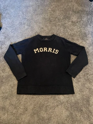 Mörkblå stickad tröja från Morris - Säljer en mörkblå stickad tröja från Morris med vit text på bröstet. Tröjan har rund halsringning, långa ärmar och ribbade muddar vid ärmslut och nederkant. Hör av er vid frågor eller funderingar