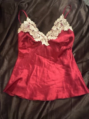 Rött satin linne med spets - Rött vintage satin linne med v-ringning, spets detalj fram, och bak resår. Funkar som nattlinne och till annat. Det står inget märke. Hör av er om frågor! ❤️