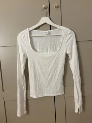 Vit långärmad topp med fyrkantig ringning - Snygg vit långärmad topp med fyrkantig ringning och tight passform. Perfekt att styla med jeans eller kjol för en clean look. Tillverkad i mjuk bomull som känns skön mot huden.