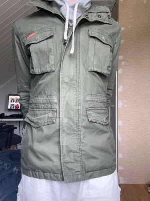 Superdry fieldjacket  - Säljer nu denna gröna fieldjackan från superdry i storlek M. Modellen är 175 väger 65kg och har storlek S. Skriv vid frågor!  Bredd 48cm Längd 70cm  Armlängd 64cm